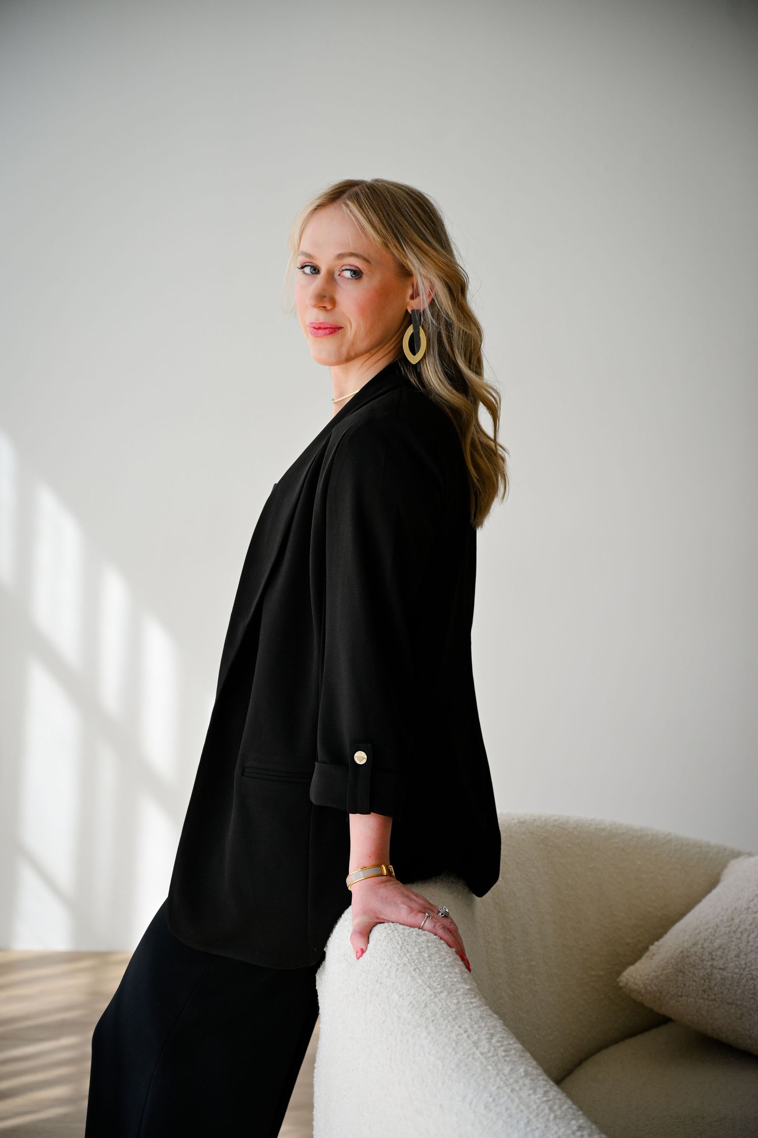 A series of artistic portraits showing a figure in a black blazer posing against a white wall with dramatic lighting.