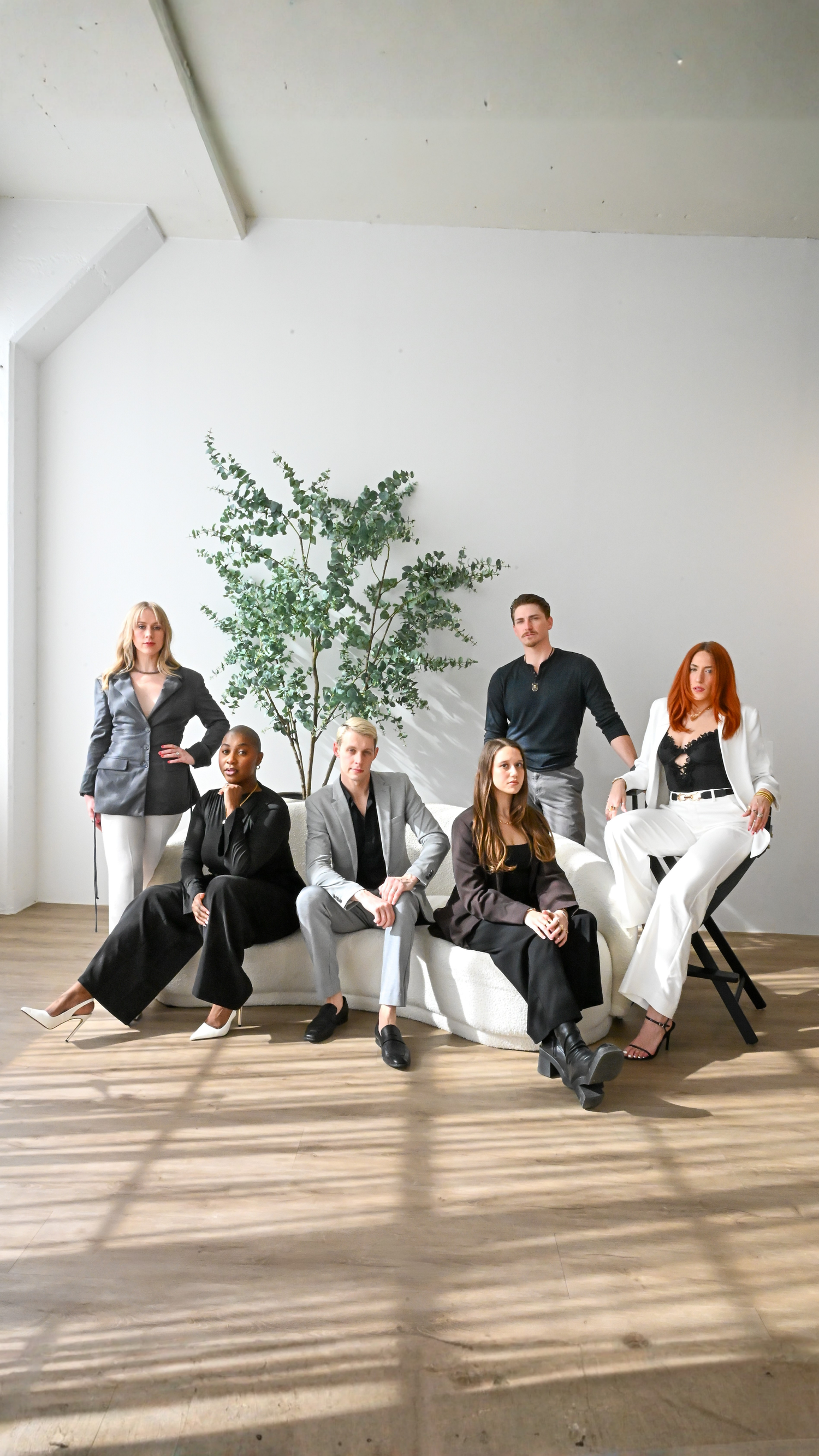 A series of artistic photos showing people sitting casually against a white wall in a minimalist studio setting.