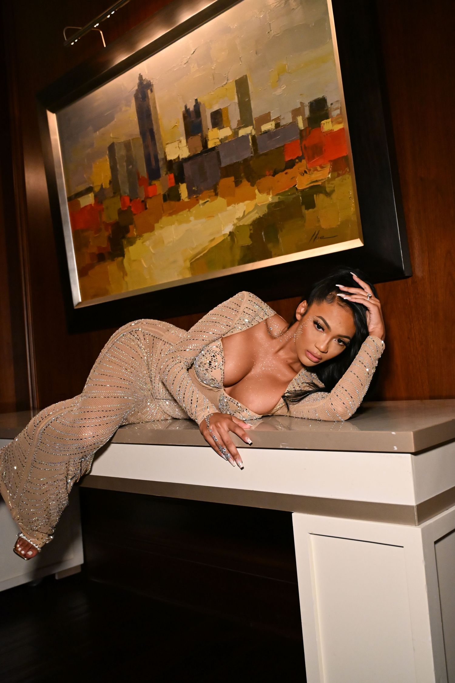 A person in a sparkly long-sleeved dress poses dramatically across a white display pedestal in an art gallery.