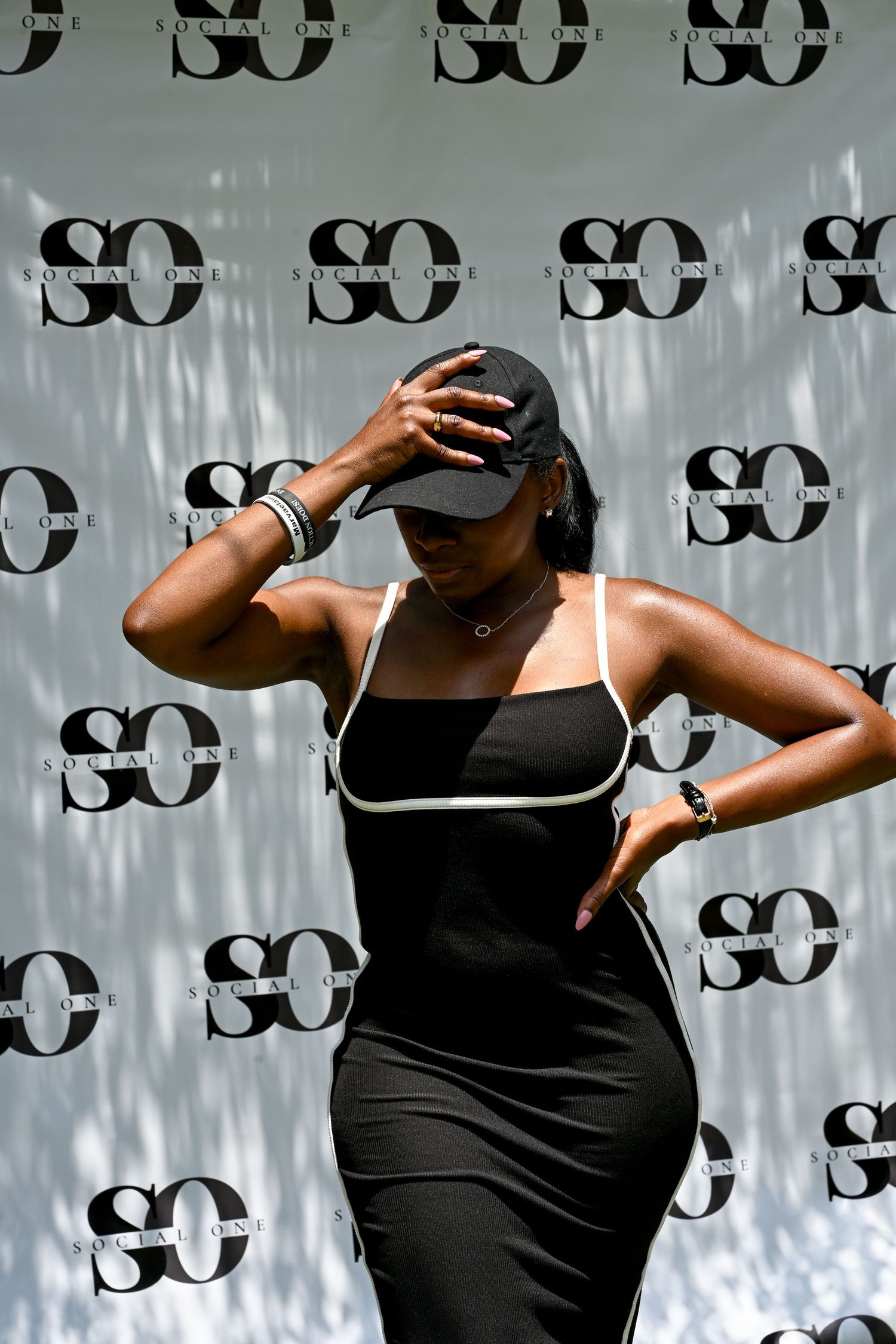 Woman in black dress and cap posing confidently at a Social One event backdrop.