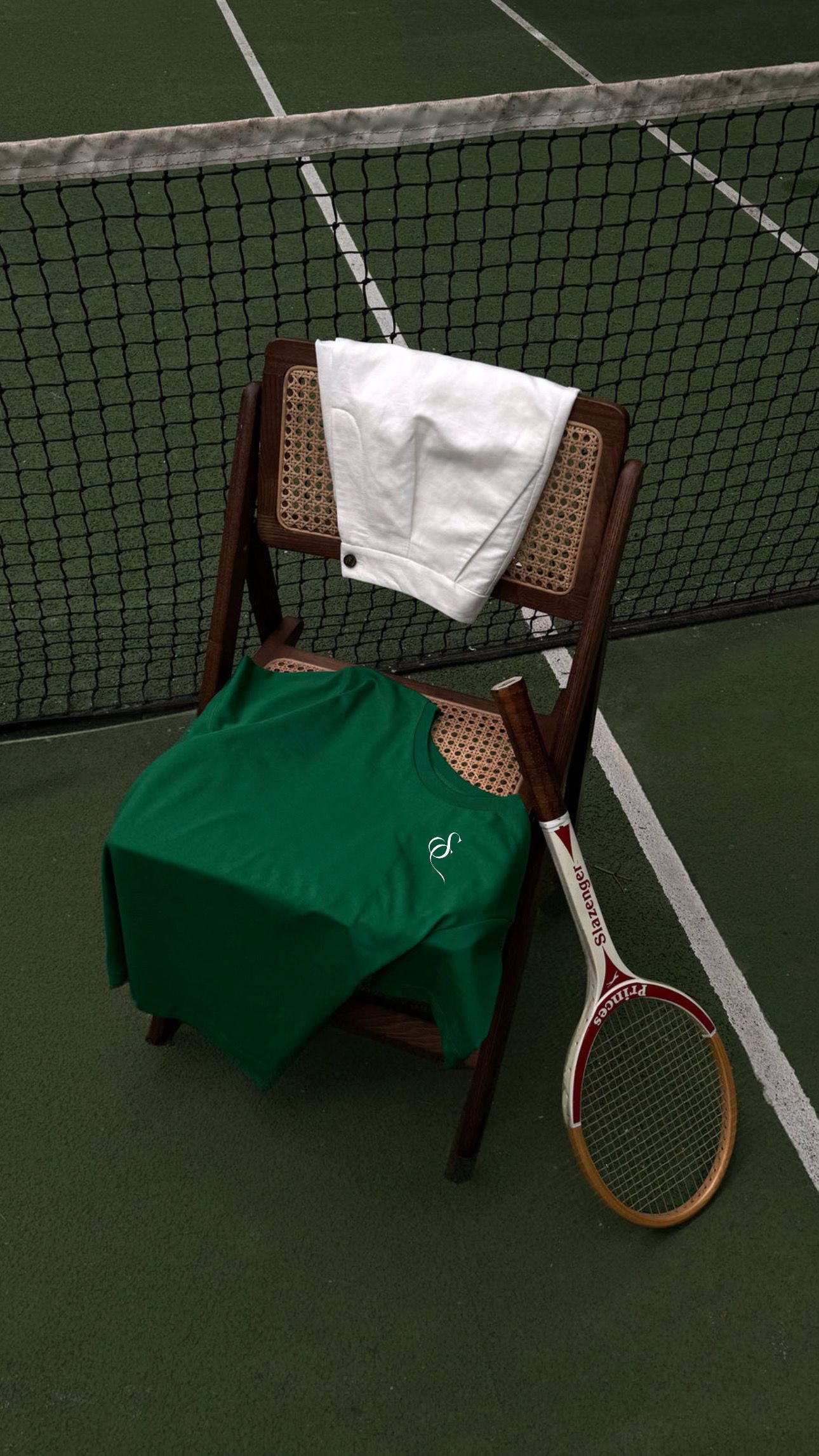 Tennis racket leans against wooden chair with white towel and green cloth on indoor court near net.
