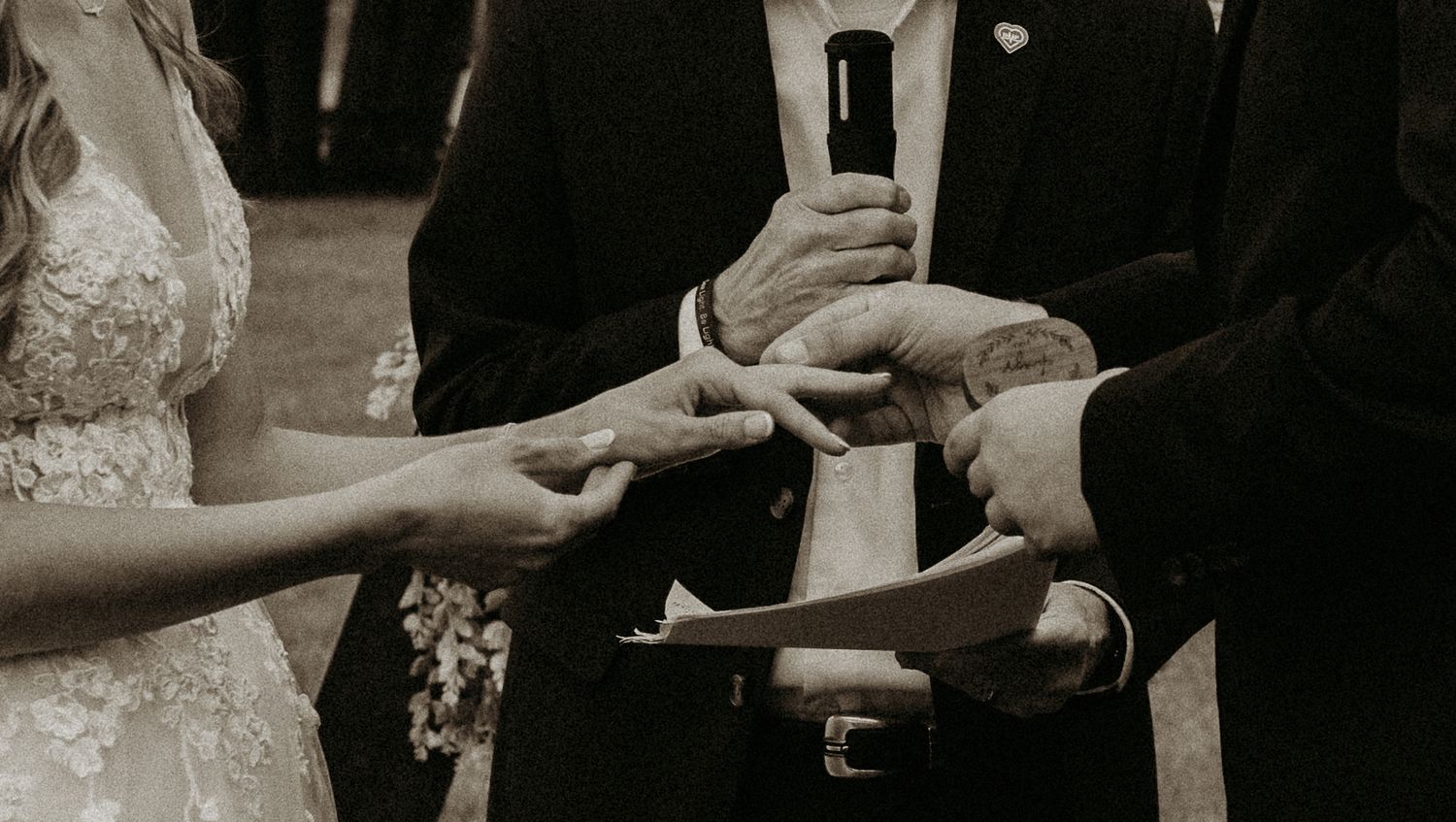 Close-up of hands exchanging rings during wedding ceremony in black and white.