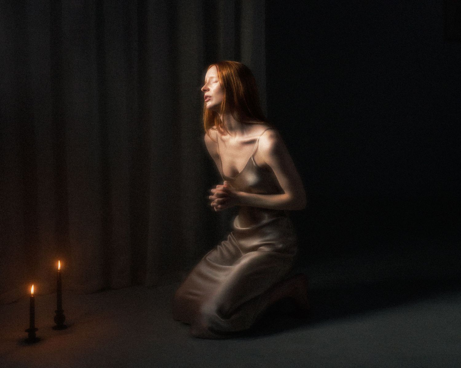 Woman in silk slip dress kneeling by candlelight in dark dramatic fine art photograph.
