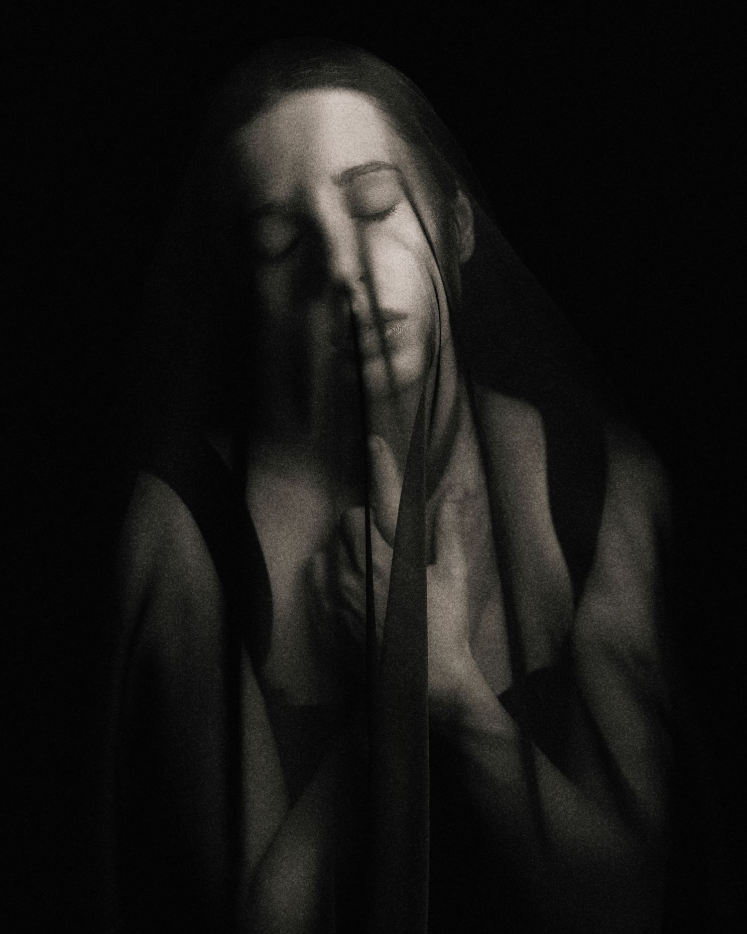 Ethereal double-exposure black and white portrait of a woman with closed eyes in dark setting.