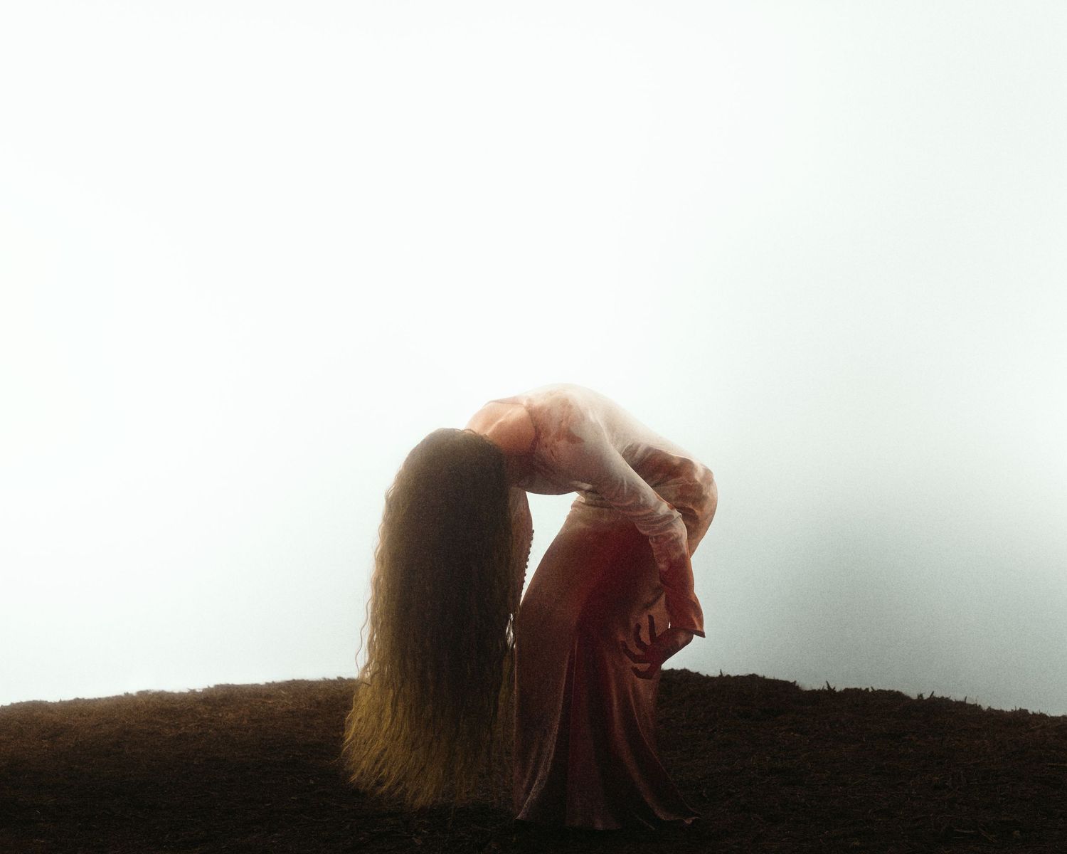 Woman in red dress bending forward with long hair falling over face against misty white sky.