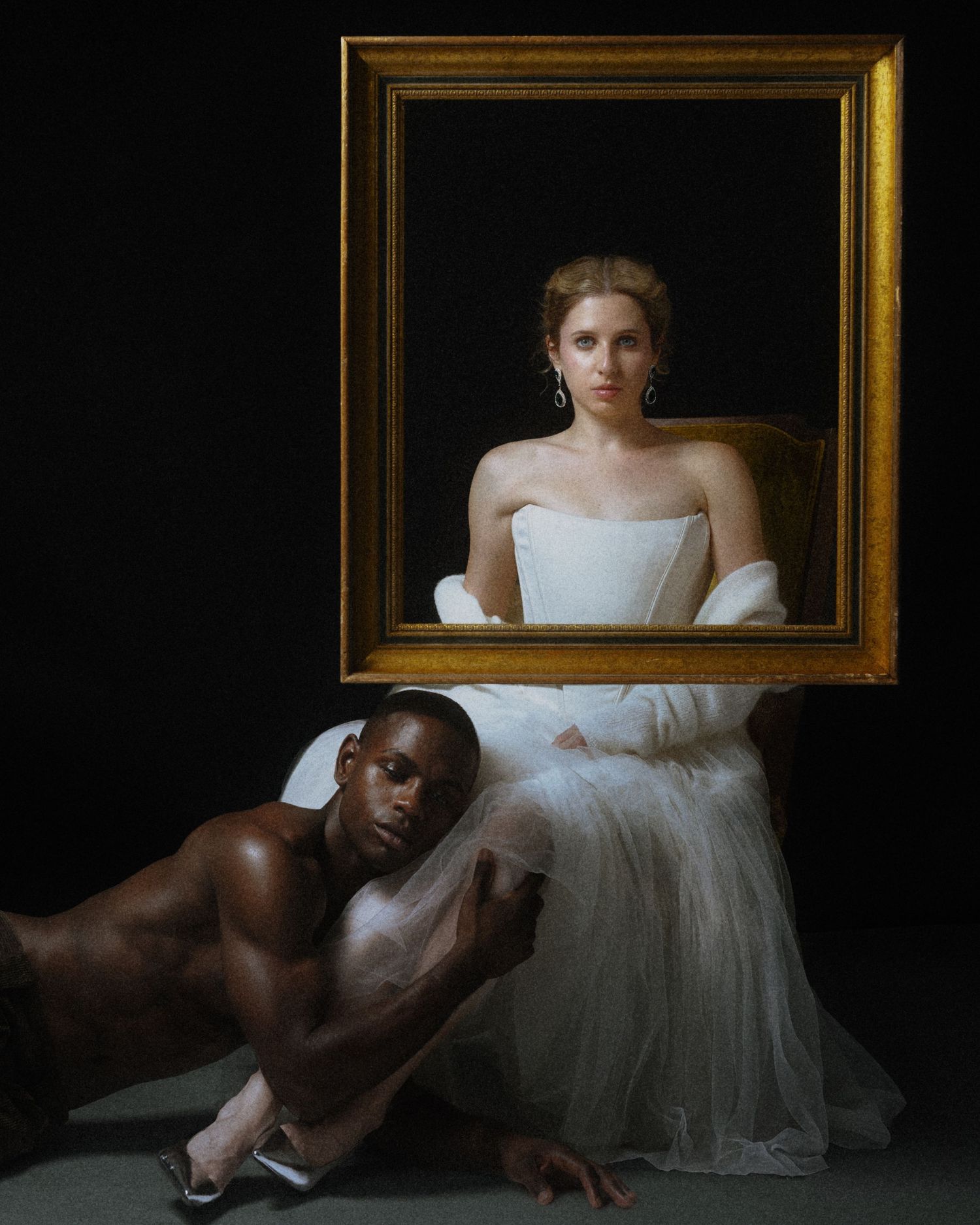 Two people posing with ornate gold frame in dramatic fine art portrait against dark background.
