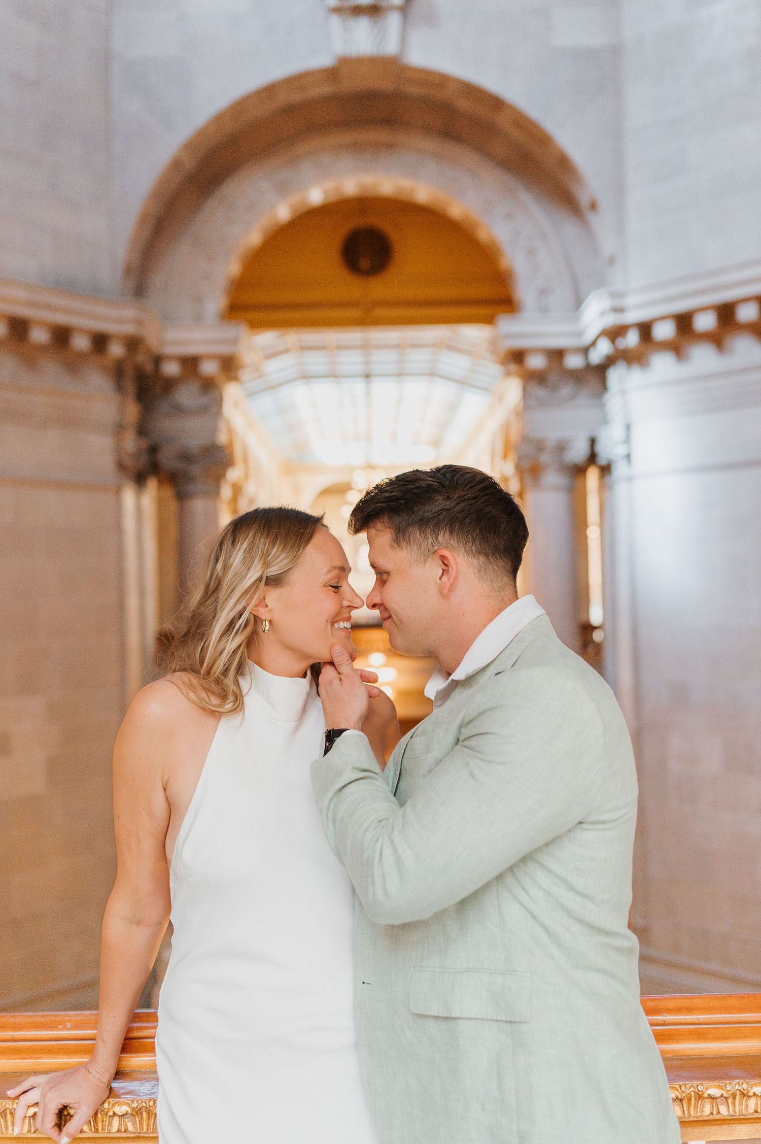 A smiling couple in wedding attire shares an intimate moment in a grand marble building interior.