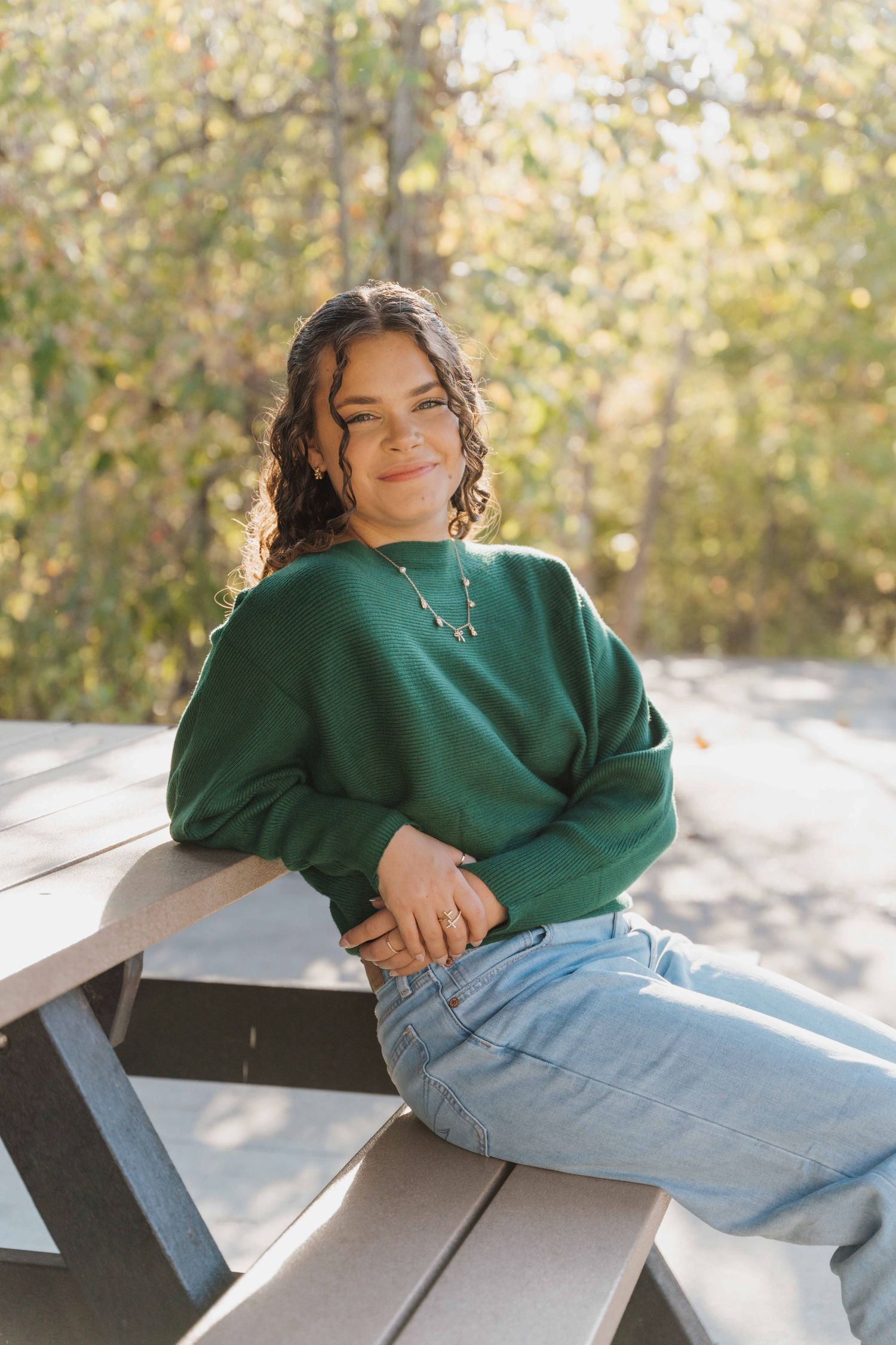 Person in green sweater and light jeans lounges casually on wooden bench in sunny outdoor setting.