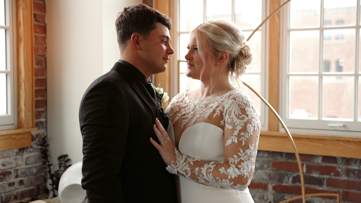 A couple shares intimate moments in a sunlit room with exposed brick walls and large windows.