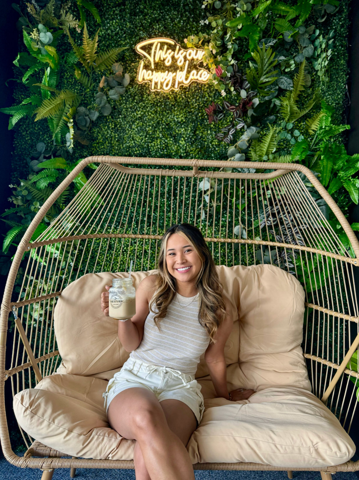 Cozy outdoor seating area with hanging rattan chair and lush greenery backdrop illuminated by neon signage.