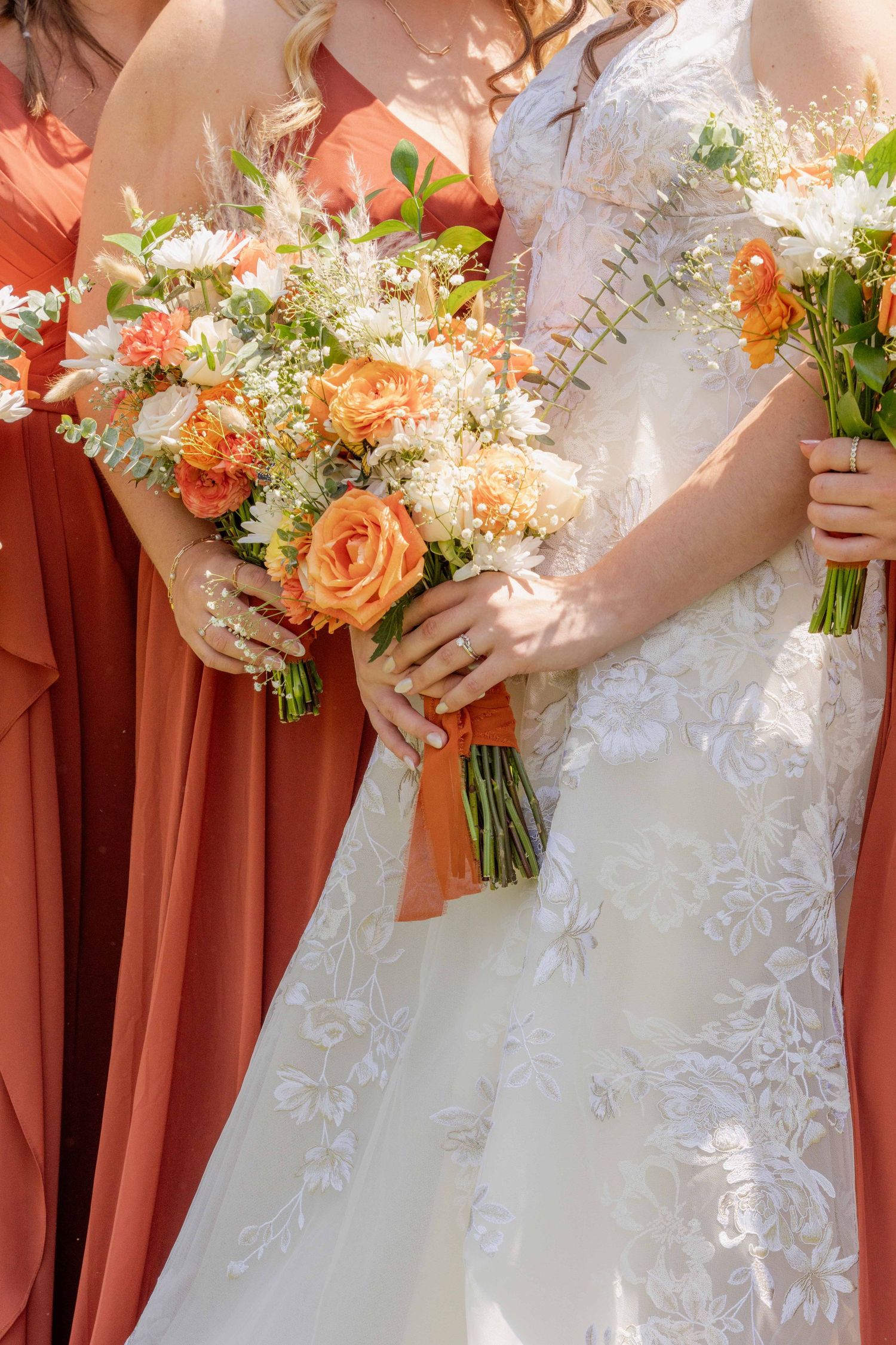 Wedding bouquets with peach roses and white flowers held against coral bridesmaid dresses and white lace gown.