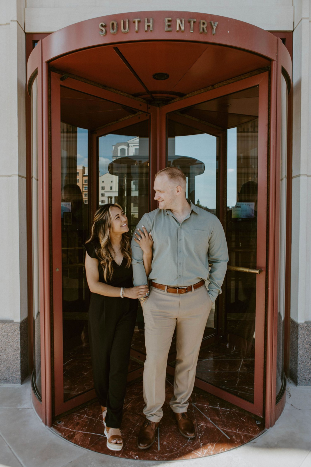A couple shares a romantic moment while standing in a revolving door entrance marked 'South Entry'.