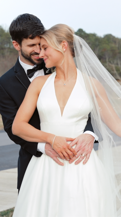 A romantic wedding portrait of a couple embracing, with the bride in a white v-neck dress and flowing veil.