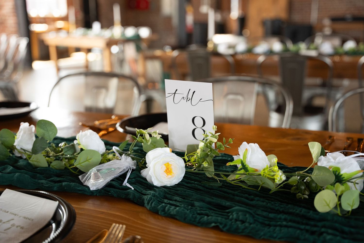 Elegant table settings with white flowers and greenery decorate a rustic wooden dining surface for a special occasion.