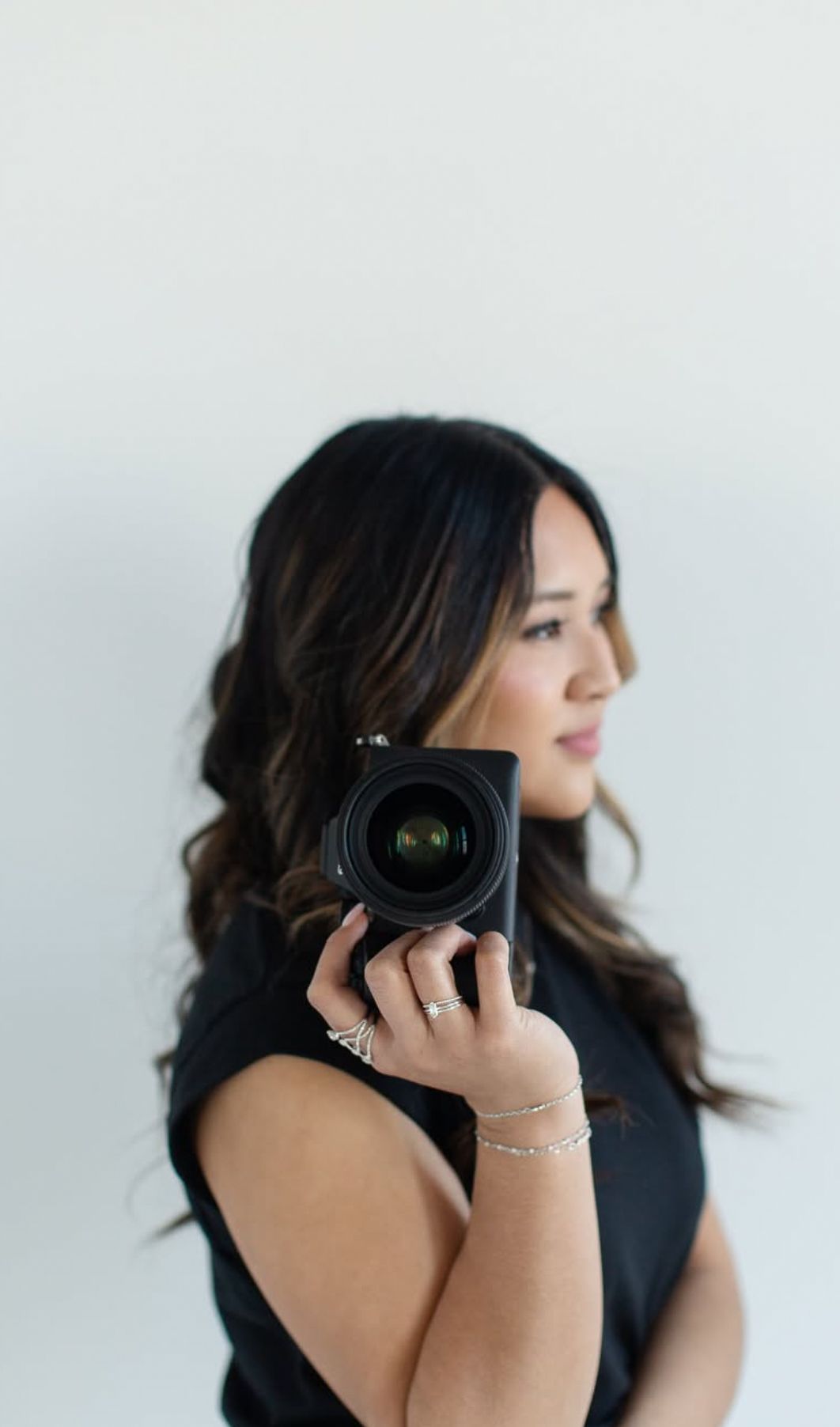 A photographer in a black sleeveless top poses with a camera against a white background in a series of artistic shots.