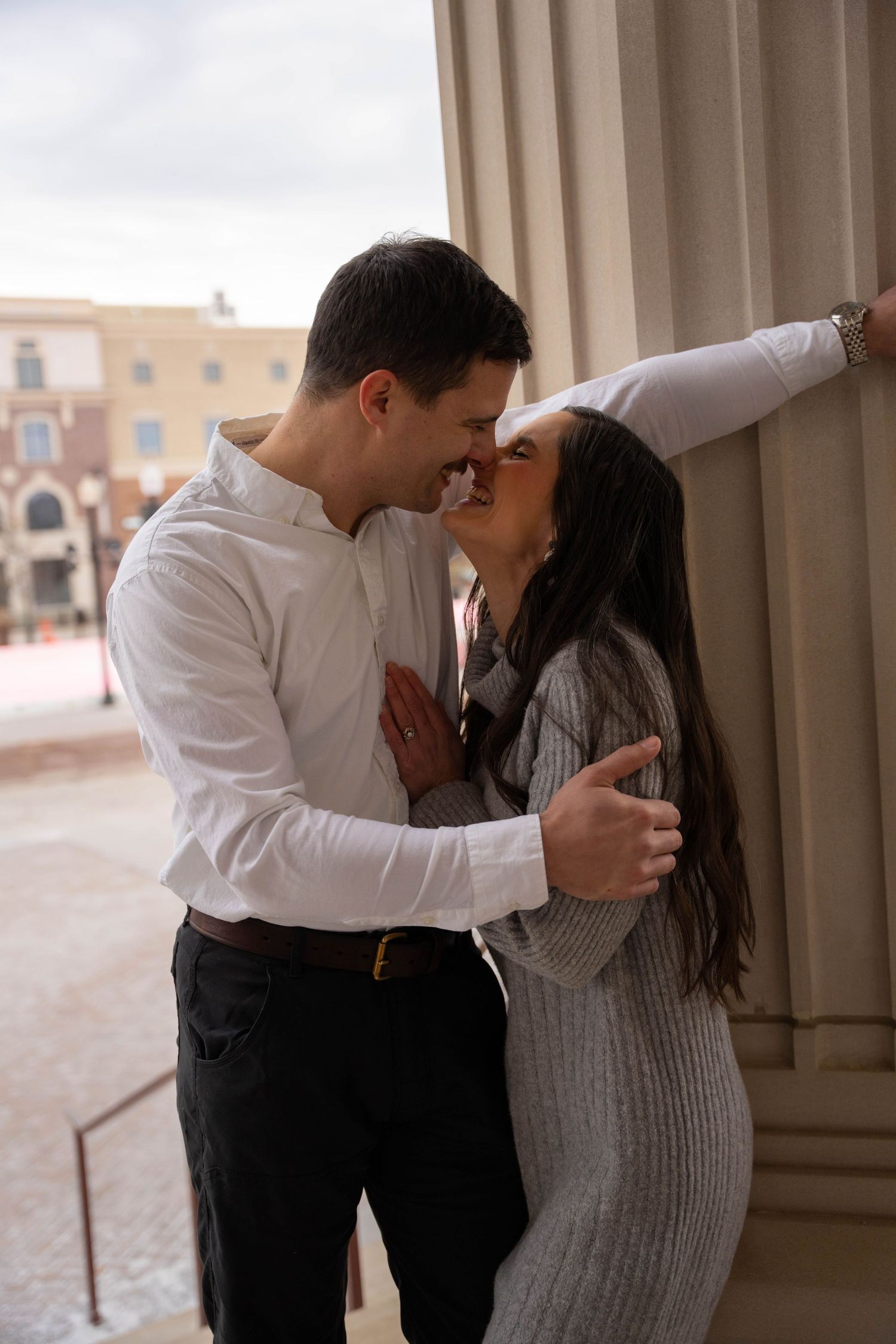 A romantic couple embraces and kisses in a series of four connected photos against a light colored architectural backdrop.