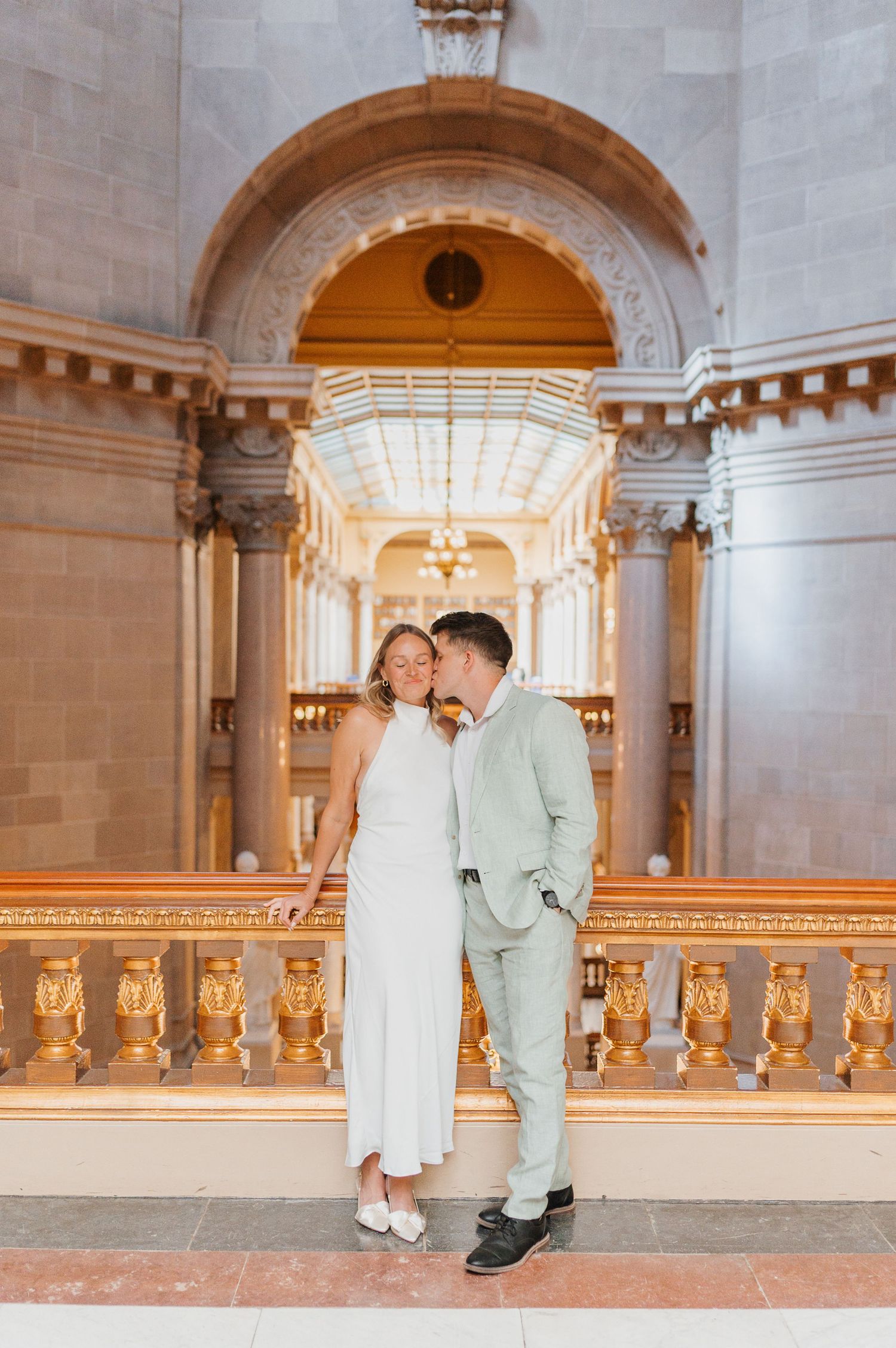 Couple in wedding attire sharing a romantic moment inside an ornate golden hall with arched ceilings.