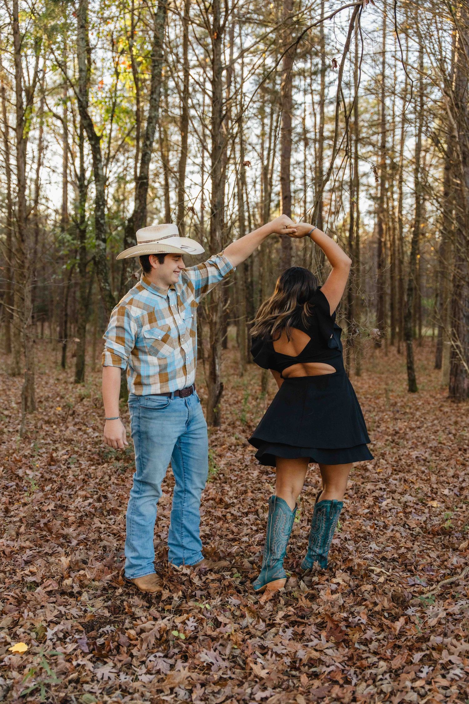 A couple dancing together in autumn woods with fallen leaves, wearing western boots and country attire.