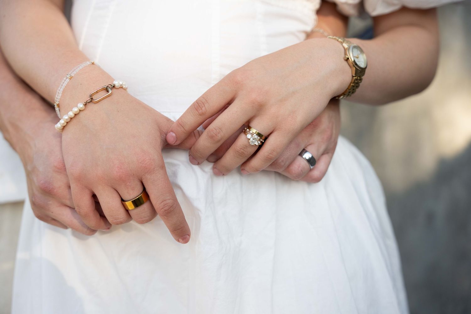 Close-up view of hands wearing elegant wedding rings against a white dress background.