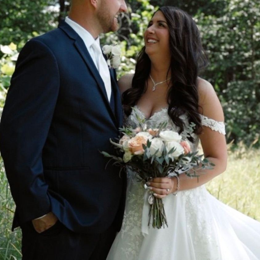 A couple in wedding attire shares intimate moments outdoors in a natural setting with sunlit greenery.
