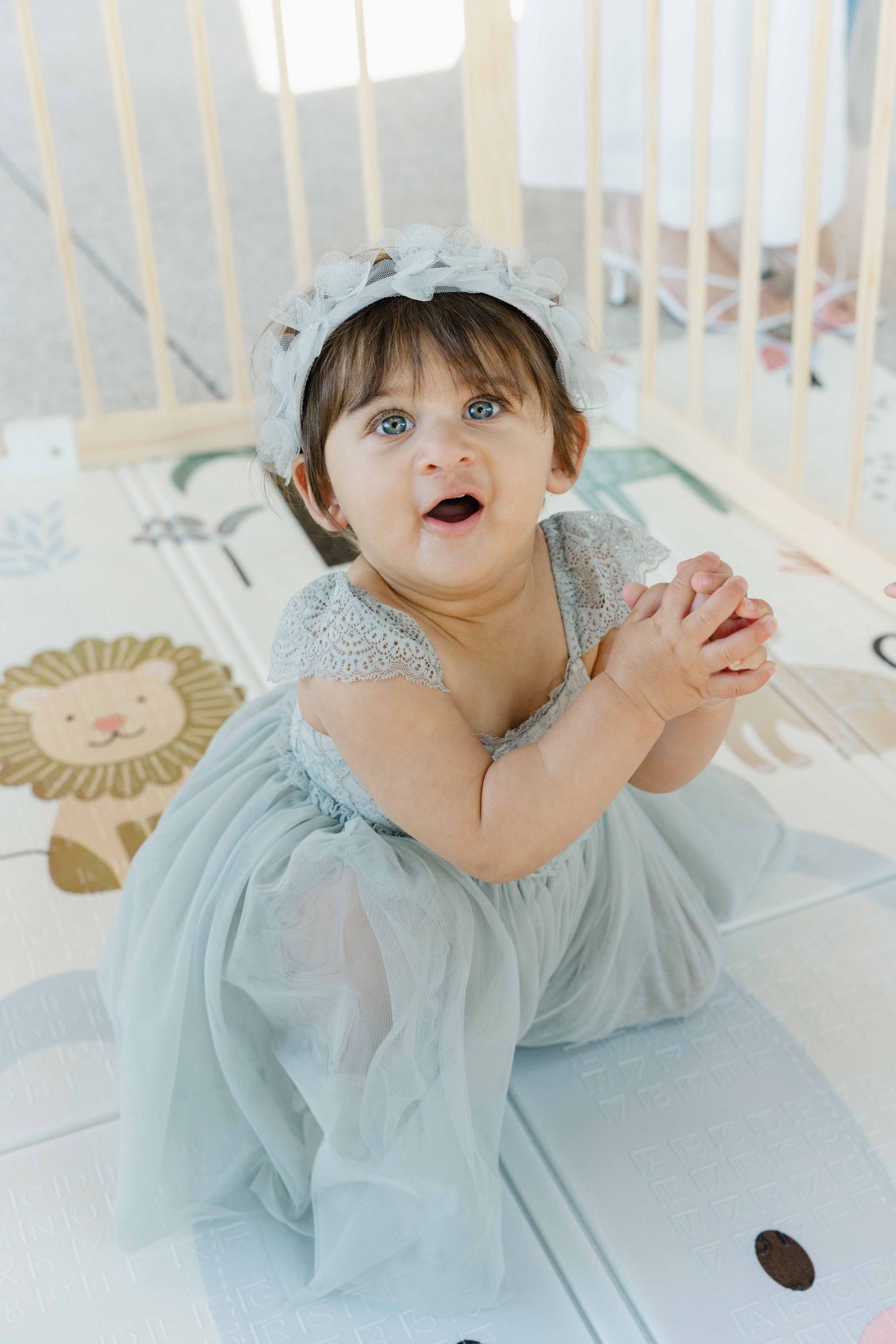 A baby in a light blue dress poses playfully in a series of four connected photos.