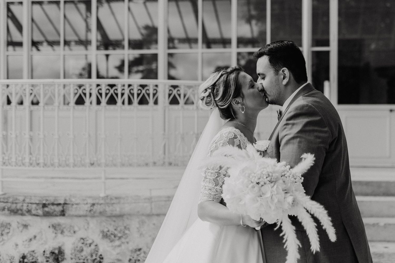 Black and white photo of bride and groom sharing a kiss holding pampas grass bouquet.