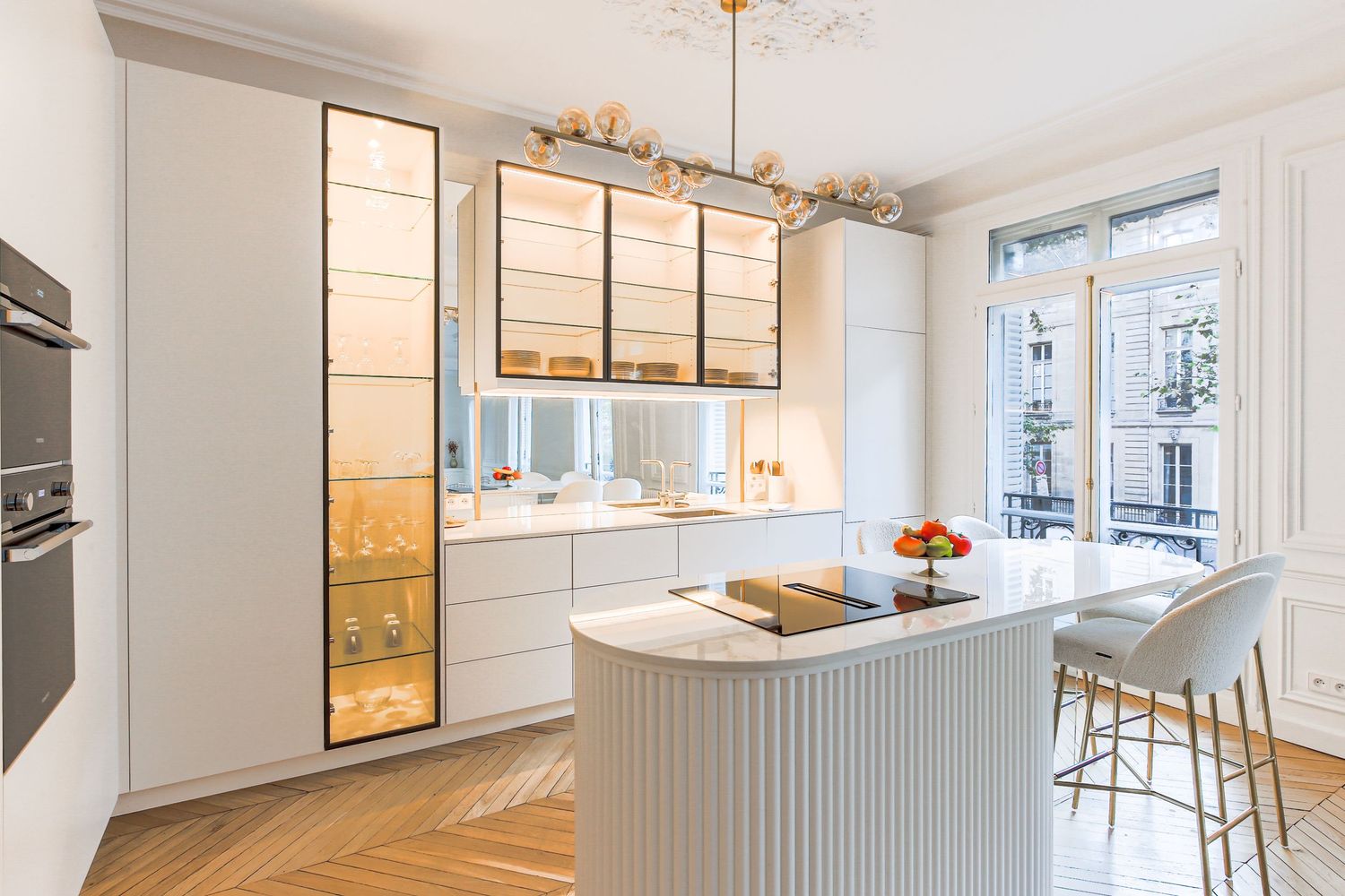 Elegant white modern kitchen with gold glass cabinets, curved island, and Parisian window view.