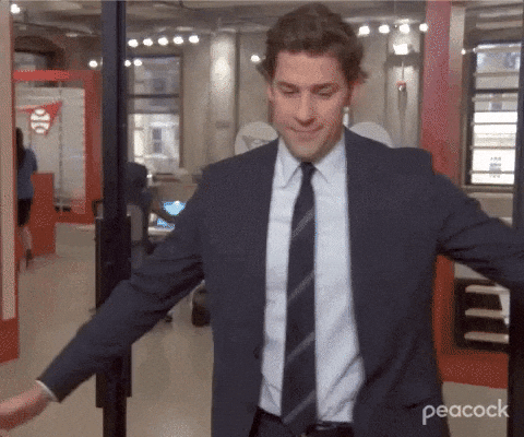 A man in a suit and tie dancing enthusiastically in a modern office setting, from The Office on Peacock.