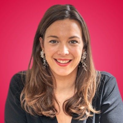 Professional headshot of a smiling brunette woman wearing elegant earrings on a red background.