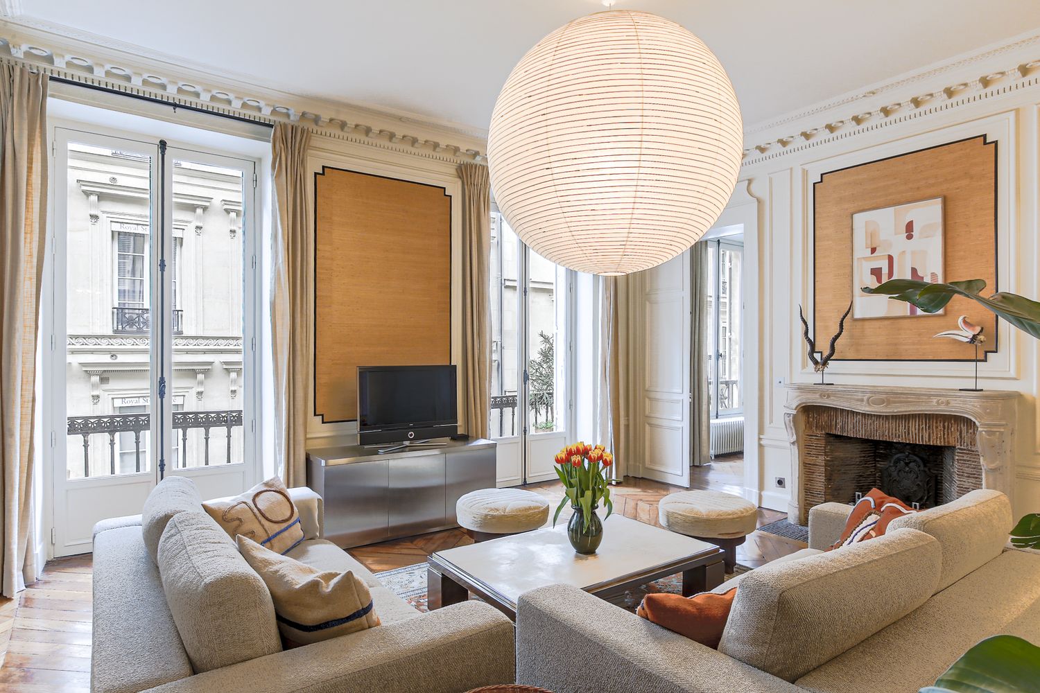 Elegant Parisian living room with high ceilings, fireplace, neutral sofas, and large pendant light.