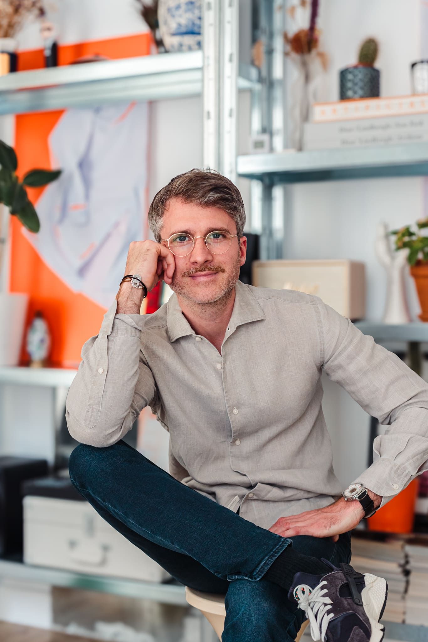 Man with glasses sitting relaxed in modern office with orange shelving.