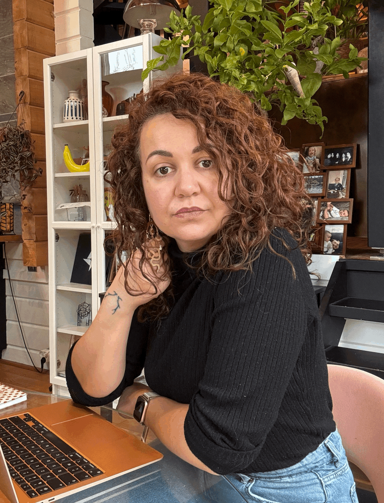 Woman with curly auburn hair sitting at laptop in cozy cafe setting.