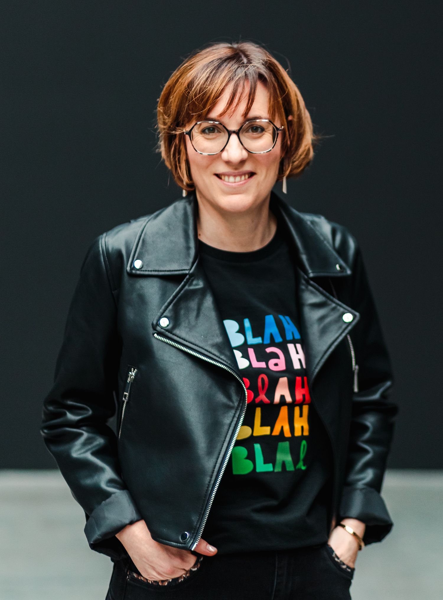 Woman in leather jacket and BLAH graphic tee posing against dark wall.