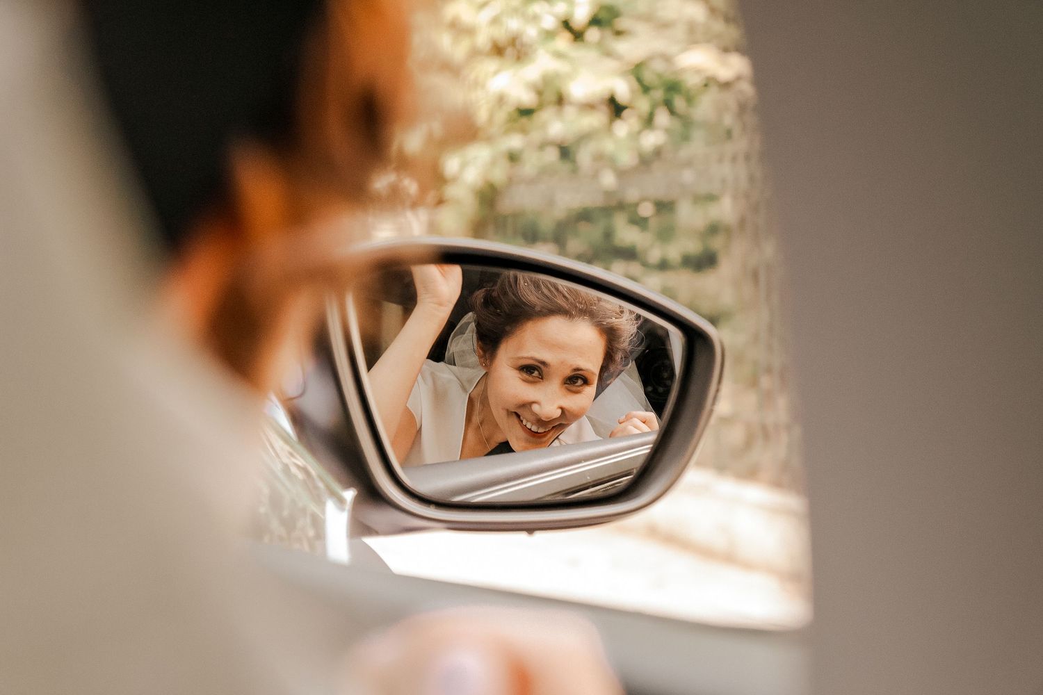Mariée souriante avec le visage qui se réflète dans le rétroviseur de la voiture.