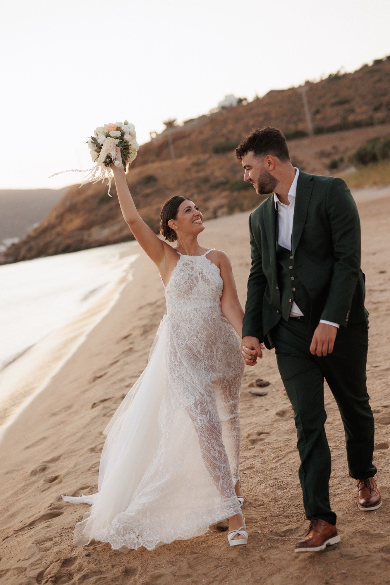 A couple in wedding attire shares intimate moments while walking along a sandy beach at sunset.