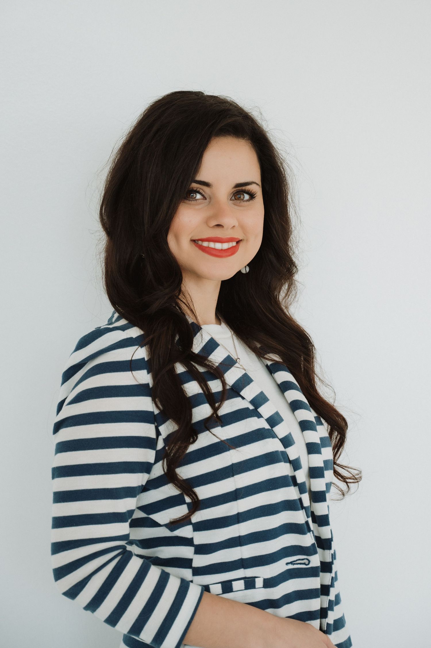 Smiling woman CPO course manager with dark wavy hair wearing a navy blue and white striped blazer against a light background.