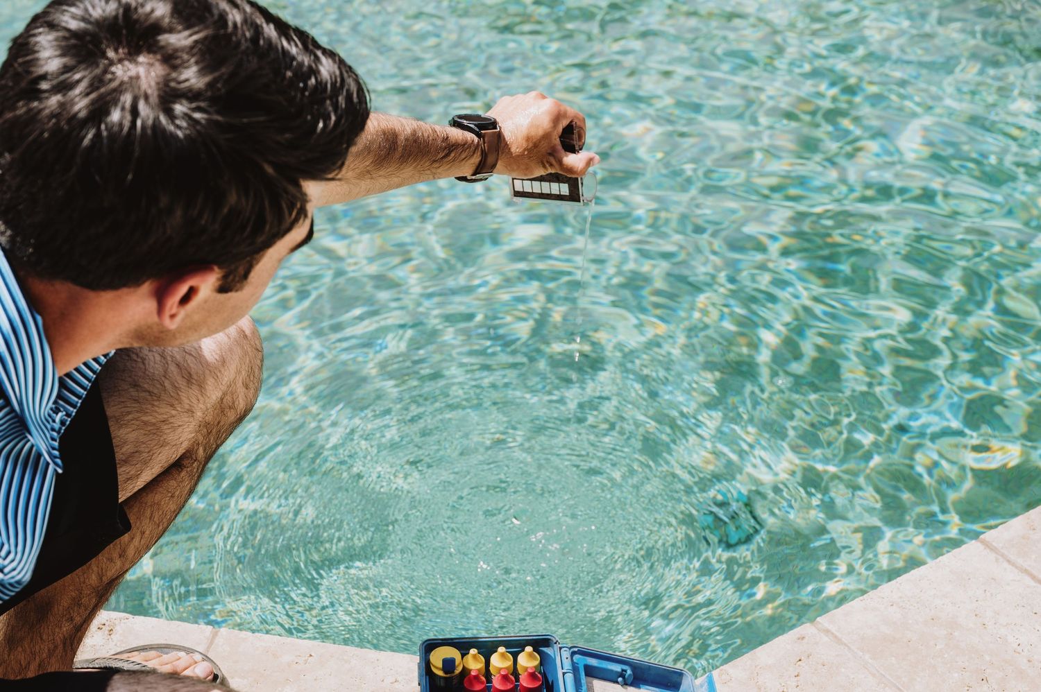 A pool technician tests water chemistry by dipping a test strip into a clear blue swimming pool.