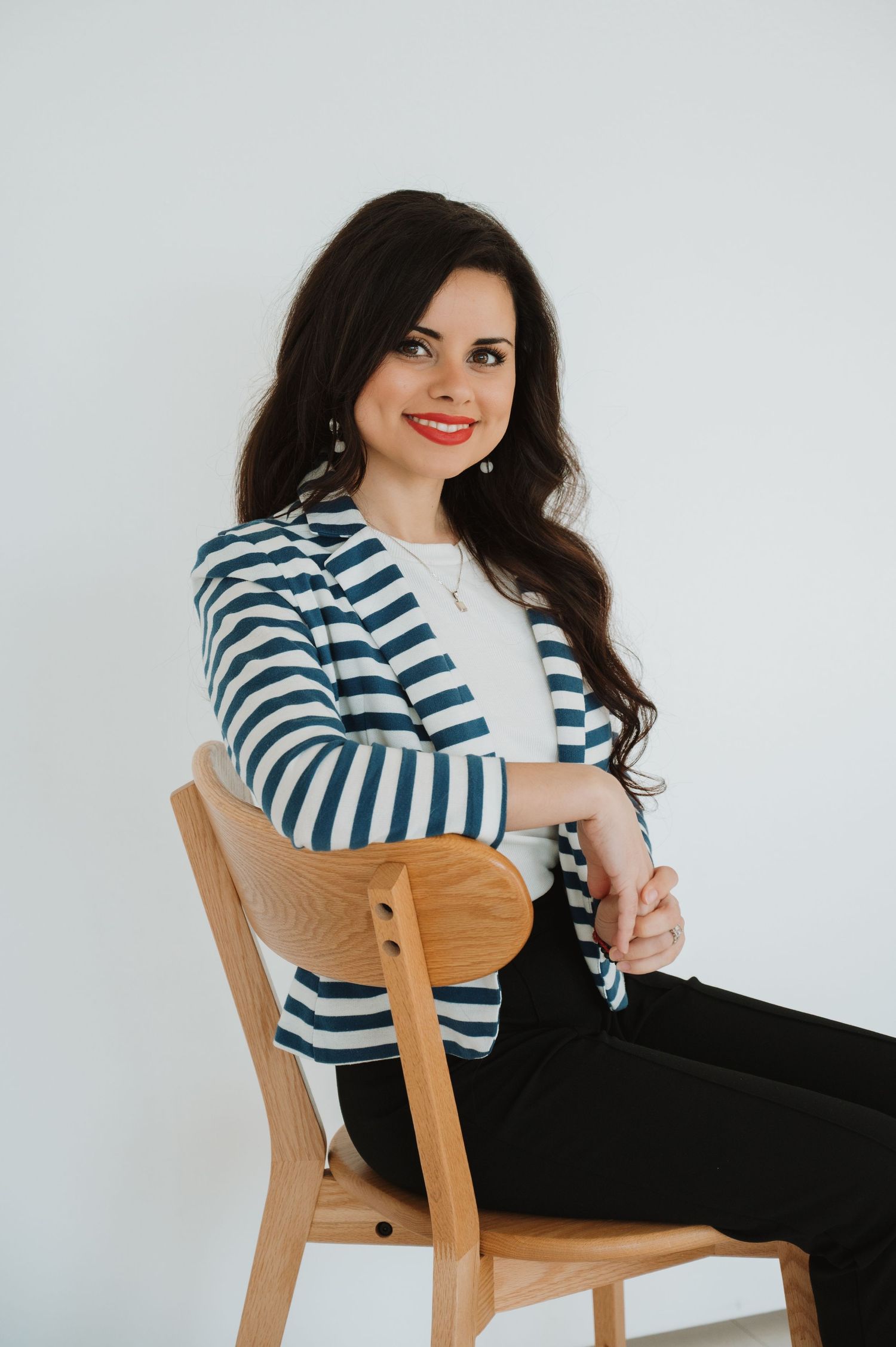 A dark-haired woman in a striped blazer sits confidently on a wooden chair ready to help you with your CPO training.