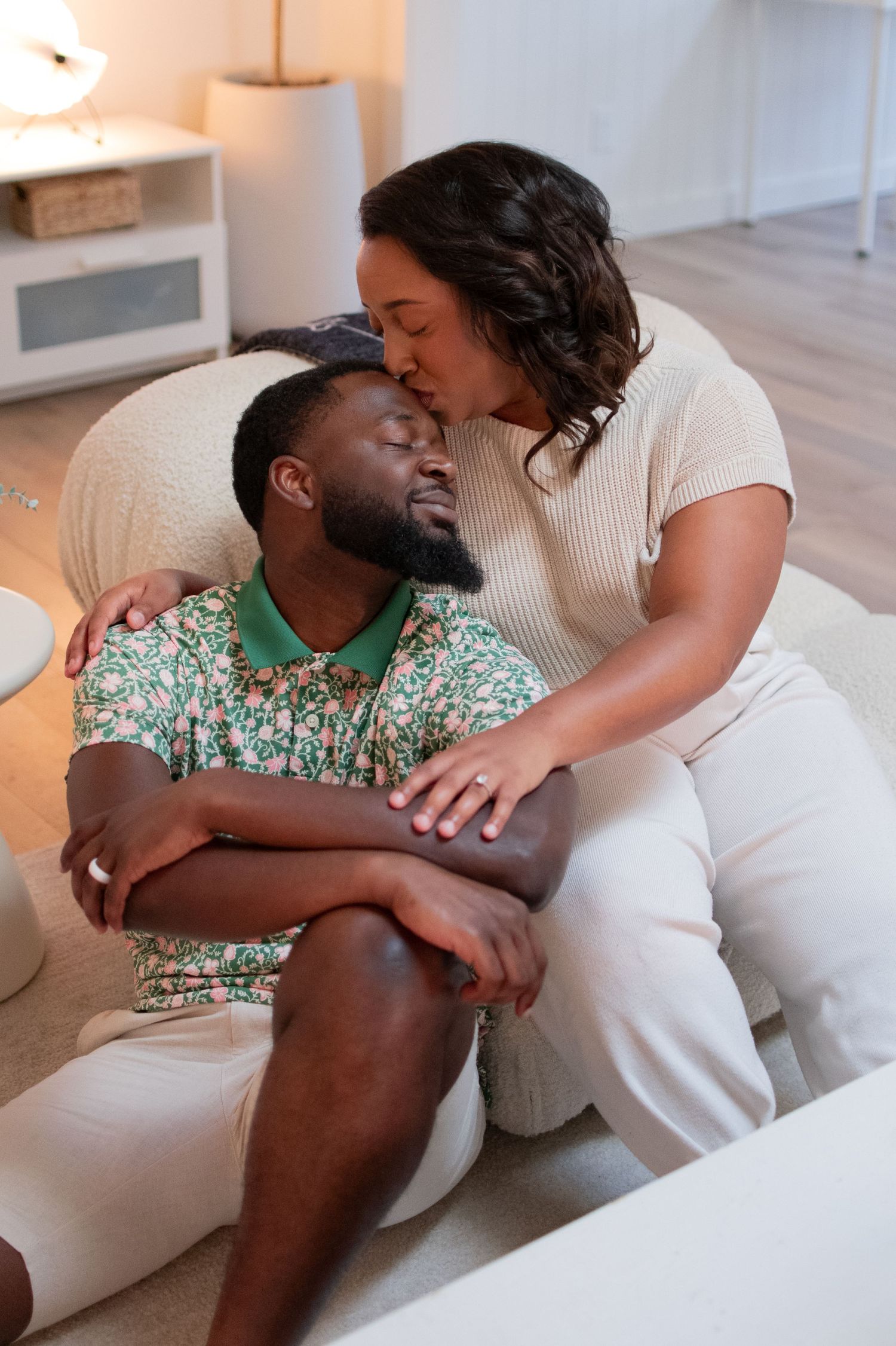 Woman kissing mans forehead while embracing on couch in cozy living room setting.