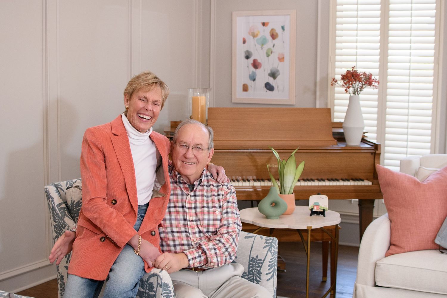 Smiling older couple posing together in elegant living room with piano in background.