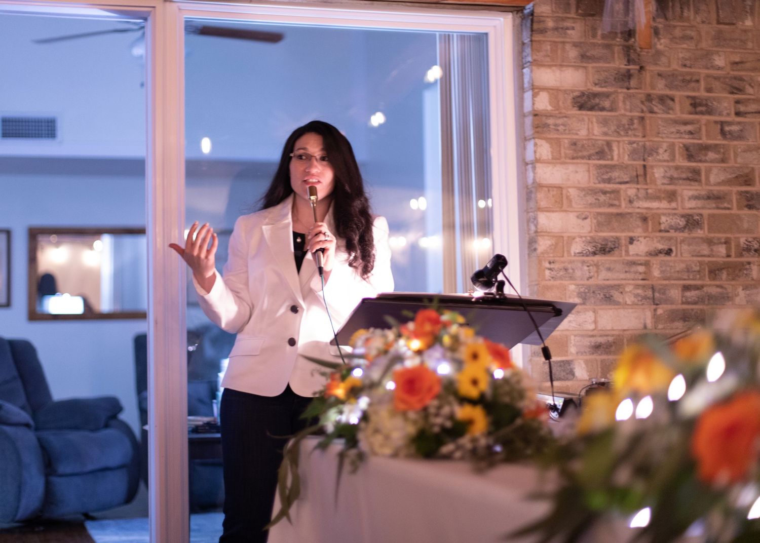 A speaker gives a presentation at a podium with floral arrangements in front.