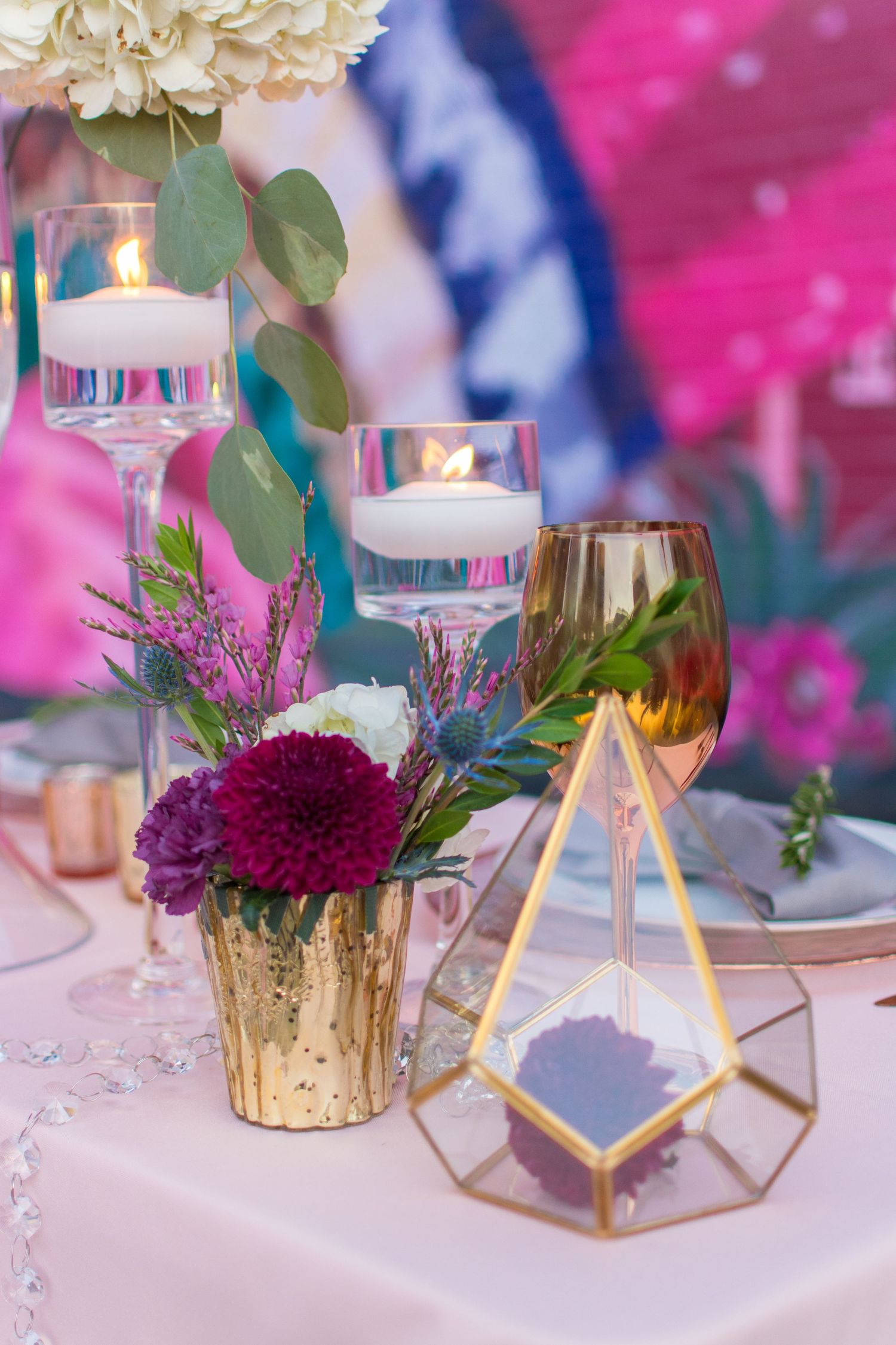 Elegant wedding table centerpiece with purple flowers, floating candles, gold vase, and champagne.