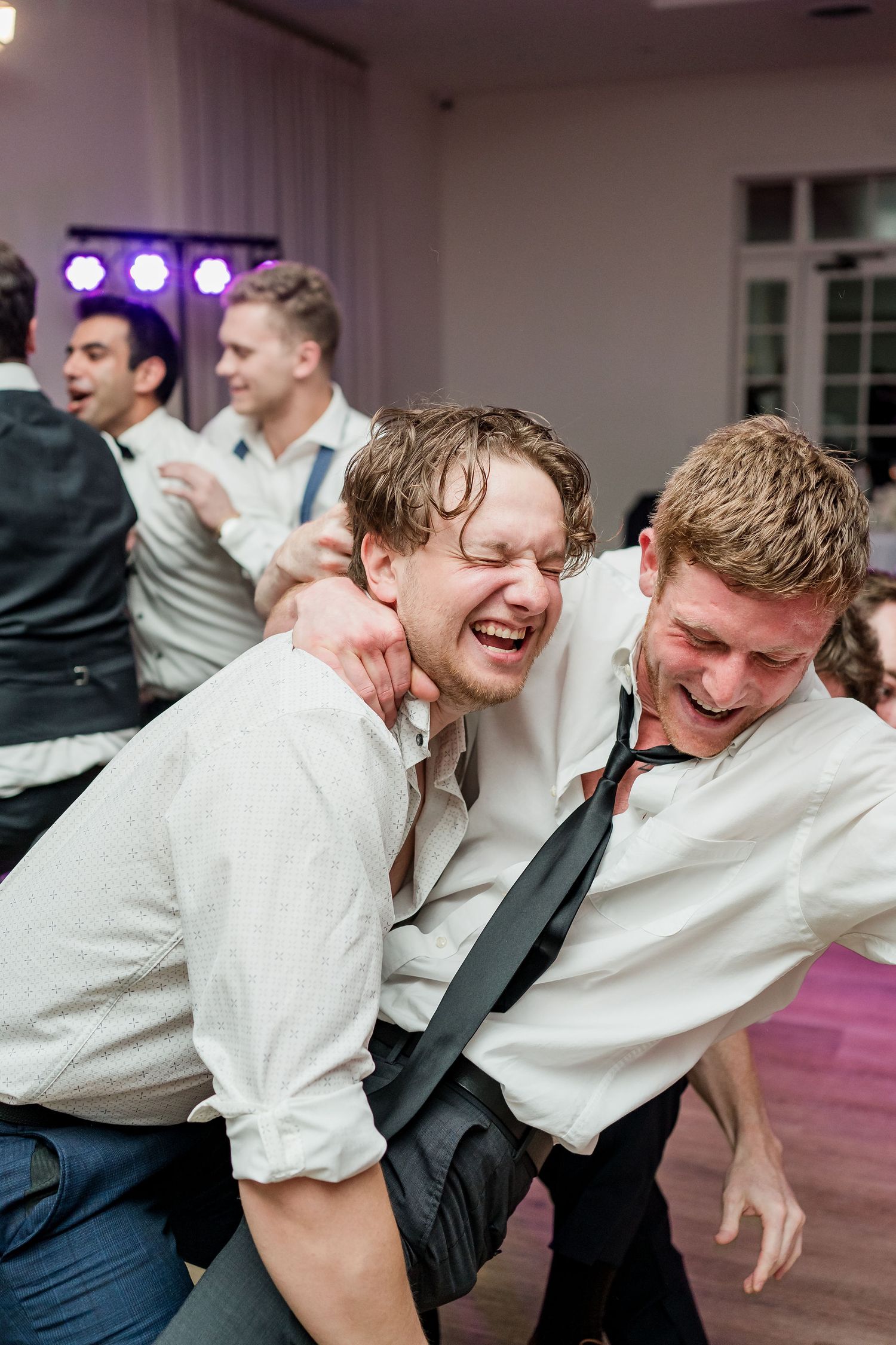 Two groomsmen laugh and dance together at a lively wedding reception party.