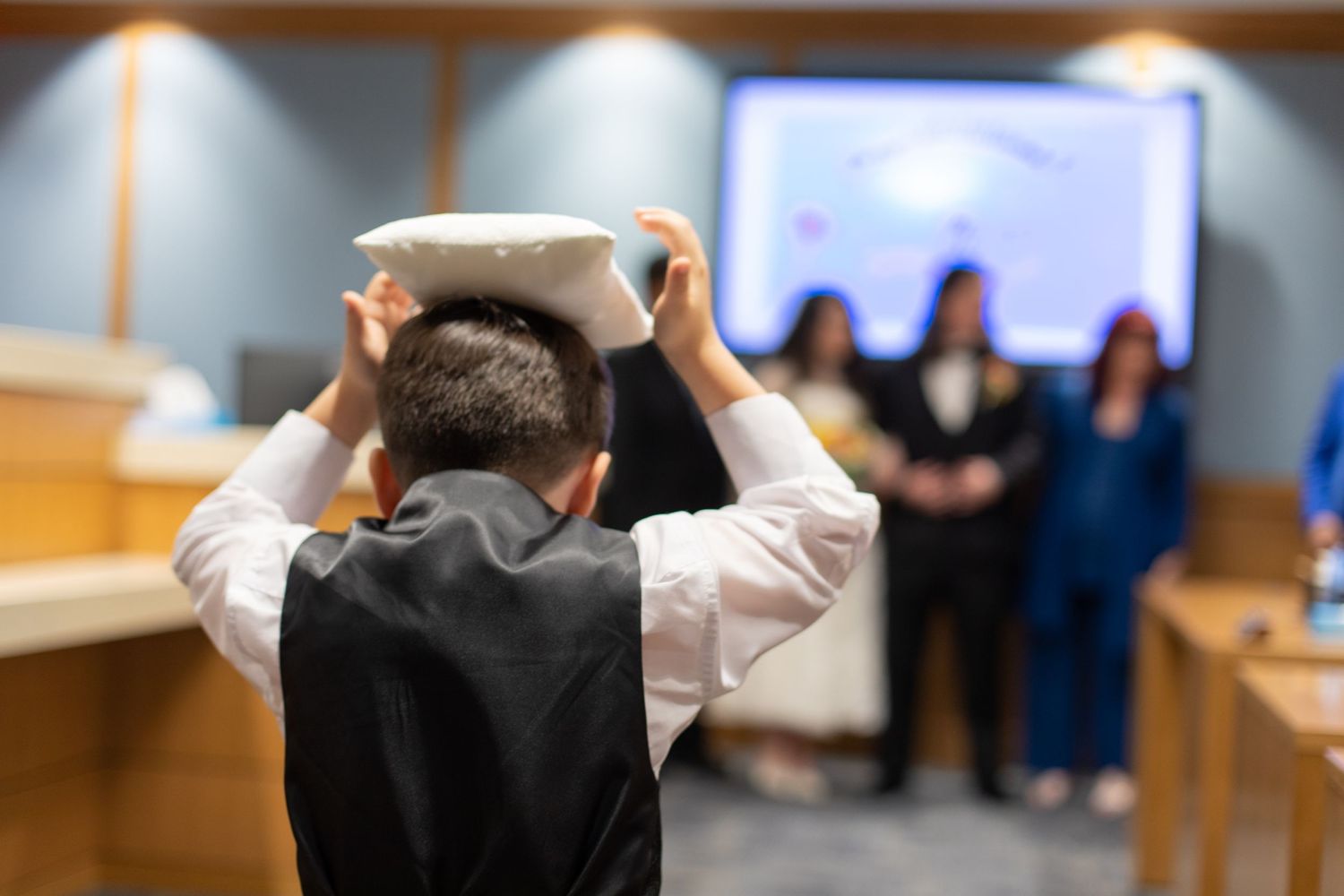 A figure in formal attire adjusts something on their head in a meeting room setting.