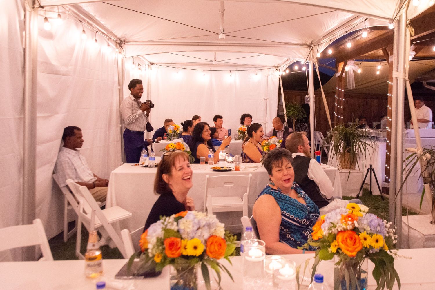 Wedding reception under a white tent with orange floral centerpieces on tables.