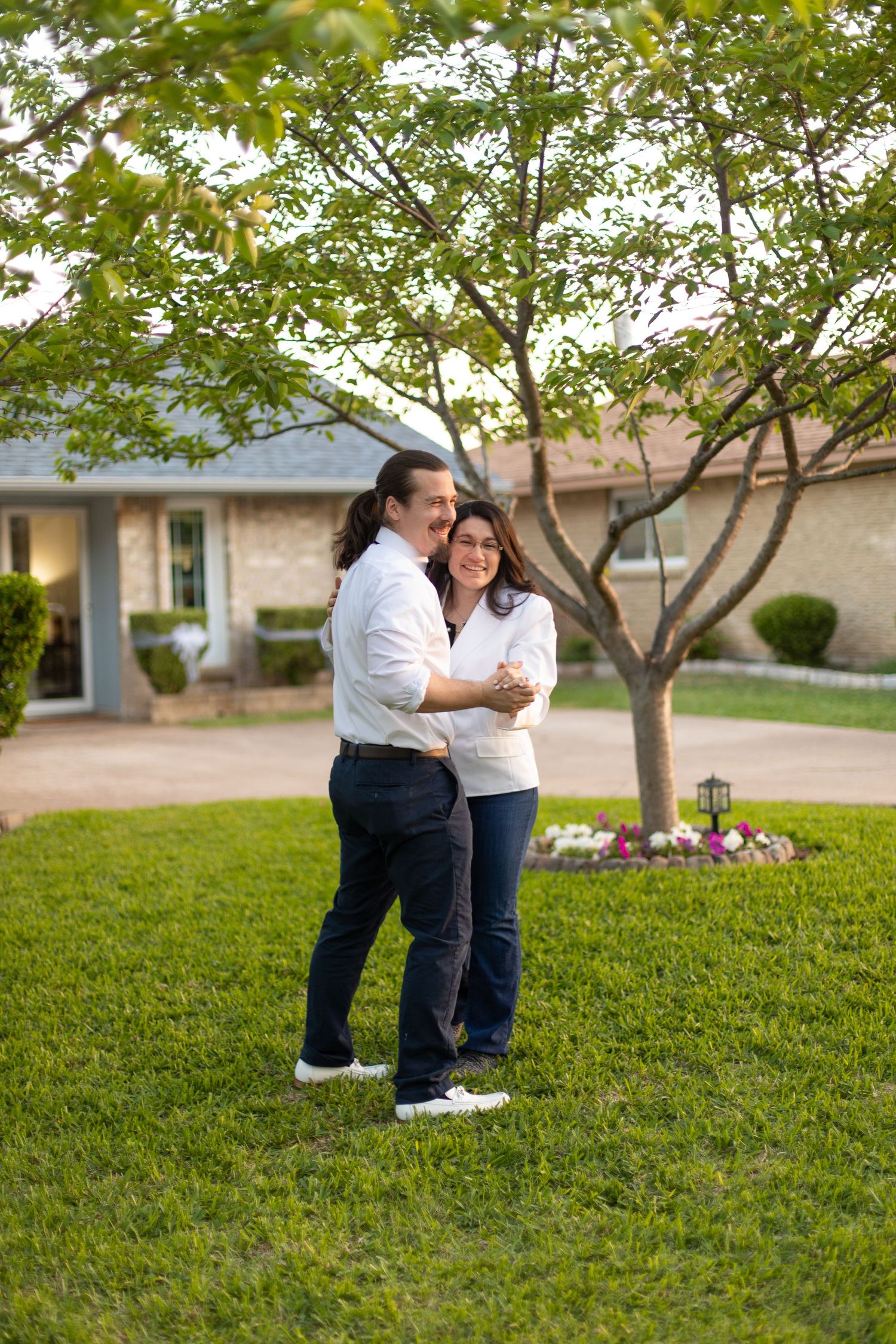 Sweet embrace while slow dancing on front lawn of brick home.