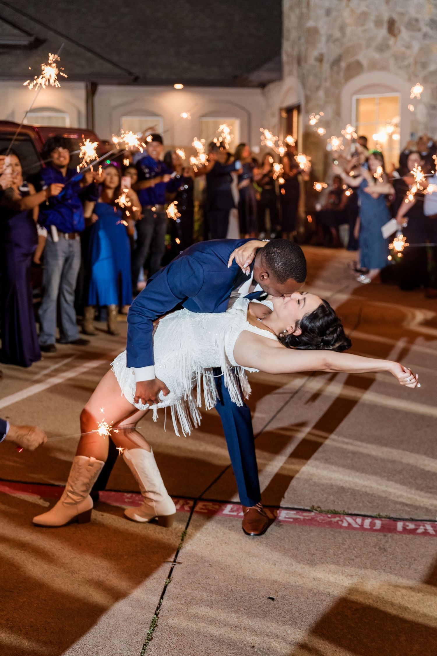 Bride and groom share a romantic dip kiss surrounded by sparklers during their wedding exit.