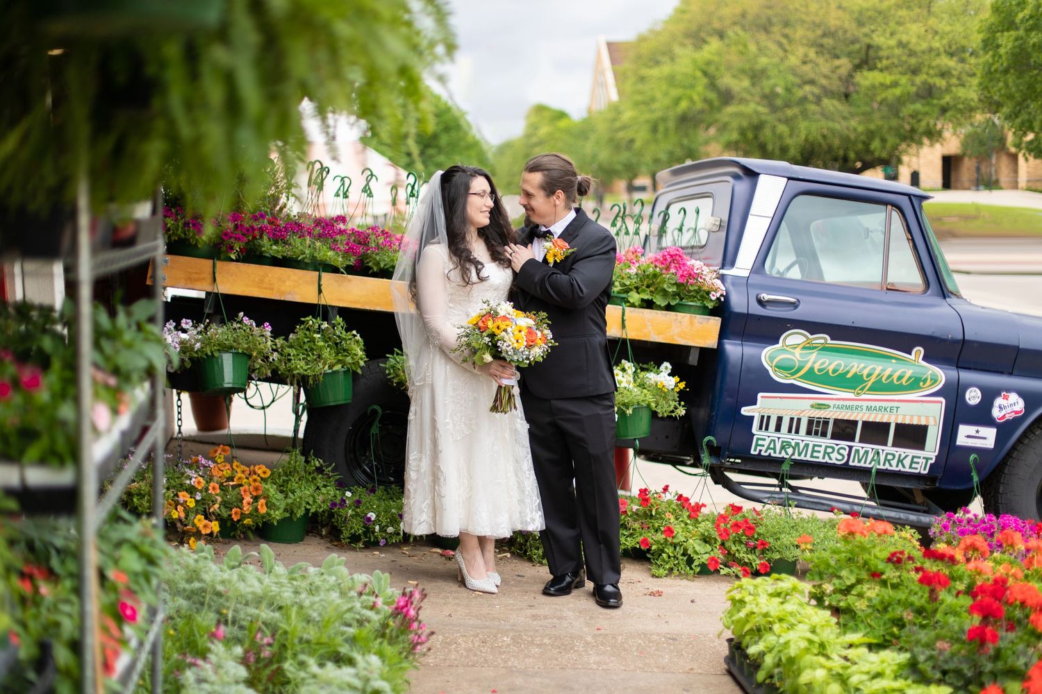 A couple shares a romantic moment in a garden nursery surrounded by colorful flowers and planters.