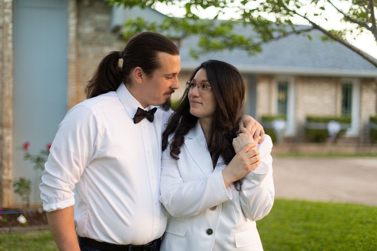 Tender moment shared between couple in formal attire on their lawn.
