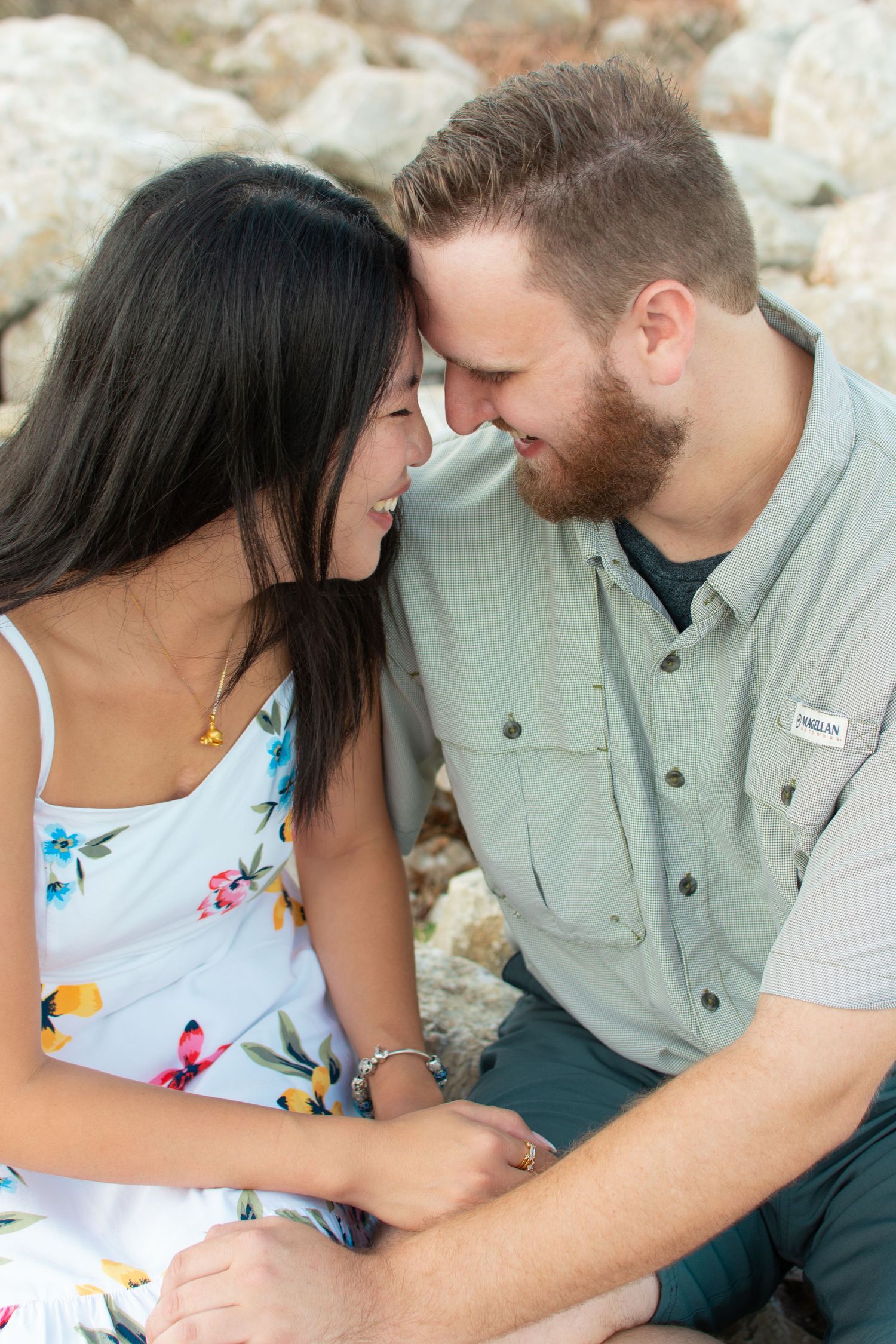 Close-up of a smiling couple touching foreheads tenderly while sitting together near rocky terrain outdoors.